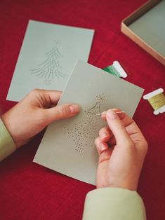 a person is making a christmas card on a table with other cards and thread spools