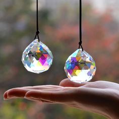 a person's hand is holding two crystal pendants hanging from strings, with trees in the background