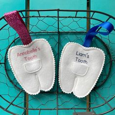 two baby bibs with name tags attached to them on a wire rack against a turquoise wall