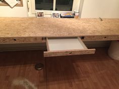 a wooden desk with drawers underneath it in front of a window and pictures on the wall