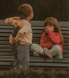 two children sitting on a bench with flowers in front of their faces, one holding the other's hand