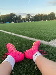 a person's feet in pink and yellow shoes on the grass at a soccer field