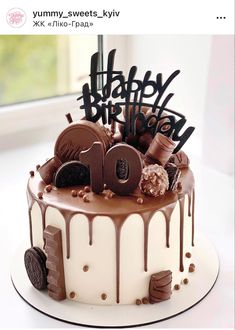 a birthday cake with chocolate icing and decorations on it's top is displayed in front of a window