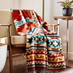 a colorful blanket sitting on top of a wooden chair next to a potted plant