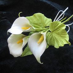 three white flowers with green leaves on a black background, in the middle of an arrangement