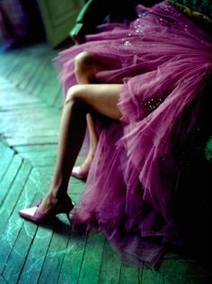 a woman sitting on top of a wooden floor next to a purple dress and shoes