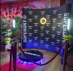 a red carpeted area with a blue screen and neon lights in the center, surrounded by plants