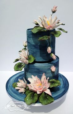 a three tiered blue cake with water lilies on the top and bottom layer