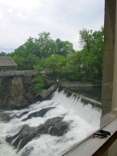 the water is rushing over the rocks in front of the bridge and house on the other side