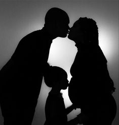 the silhouette of a man and woman kissing in front of a wall with sunlight behind them