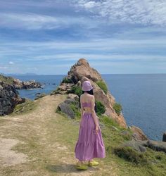 a woman in a purple dress is standing on the edge of a cliff overlooking the ocean