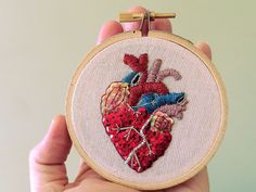 someone is holding up a cross stitch heart