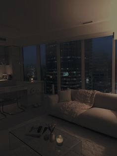 a living room filled with furniture and tall buildings in the background at night, lit by lights from windows