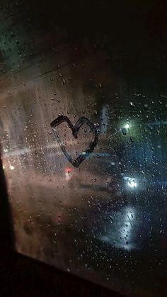 a heart drawn on the side of a car window in the rain at night time