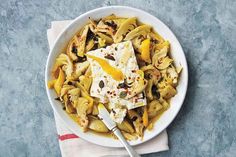 a white bowl filled with pasta and cheese on top of a blue table cloth next to a fork