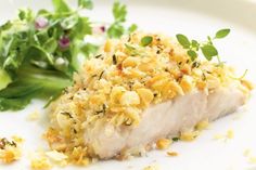 a white plate topped with fish covered in crumbs next to a green leafy salad