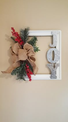 a christmas wreath is hung on the wall in front of a white frame with red berries and evergreen