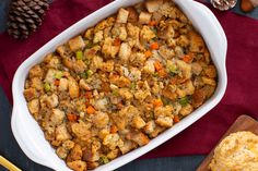 a casserole dish filled with stuffing next to a wooden spoon and pine cones