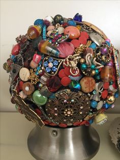 a metal vase with lots of different colored beads on it's sides and an assortment of necklaces attached to the top