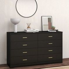 there is a black dresser with gold drawers and a round mirror on the wall above it