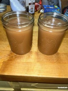 two jars filled with brown liquid sitting on top of a wooden table