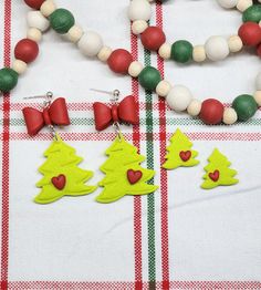 two necklaces with christmas trees on them are sitting next to some beads and bows