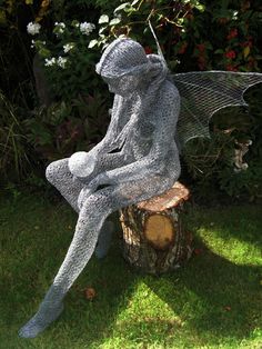 a statue of a fairy sitting on top of a tree stump in front of some bushes