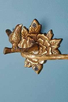 a gold bird and branch brooch pin on a light blue background, with two smaller birds perched on it's back end