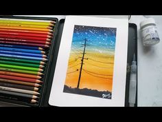 an artist's painting with colored pencils in front of it and a box of crayons next to it