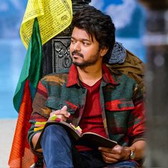 a man sitting on the ground with a book in his hand and an umbrella behind him