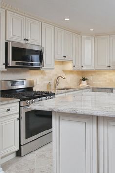 a kitchen with white cabinets and marble counter tops