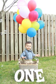 a little boy sitting in a basket with balloons