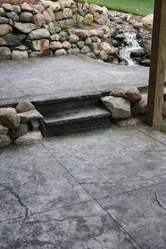 a stone patio with steps leading up to a water feature in the back yard area