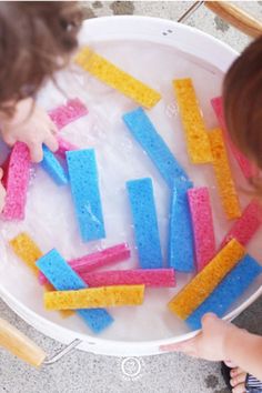 two children playing with colored sponges in a tub