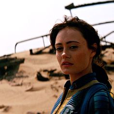 a woman standing in front of a burnt out building and looking off into the distance