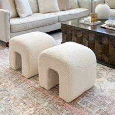 a living room filled with white couches and pillows on top of a rug next to a coffee table