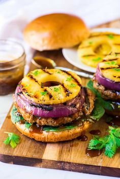 grilled burgers with pineapple and onion rings on a cutting board next to bread