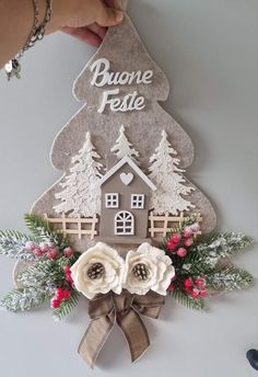 someone is holding up a paper cutout with a house and trees on it that says buone feste