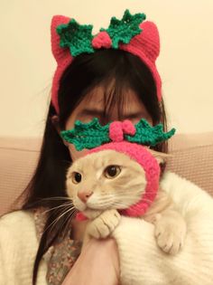 a woman holding a cat wearing a knitted hat