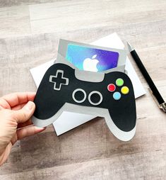 a hand holding an apple sticker with a video game controller on it and a pen next to it