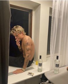 a man with tattoos sitting on a counter in front of a mirror