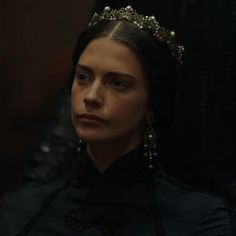 a woman wearing a tiara and earrings in a dark room with other people looking on