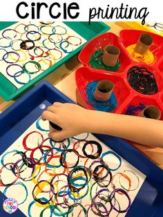 a child's hand is painting circles on a tray with colored paper in front of them