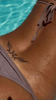 a woman with a tattoo on her back laying in the water next to a swimming pool