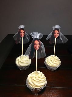 three cupcakes with white frosting and two heads on sticks