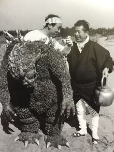 two men standing next to each other near a giant creature holding a teapot in his hand