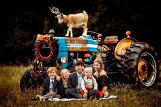 a family poses in front of an old tractor with a goat on top and two young children