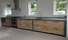 an empty kitchen with wooden cabinets and stainless steel appliances on the counter tops, in front of two windows