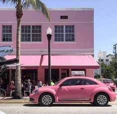 a pink car parked in front of a building with palm trees on the side walk