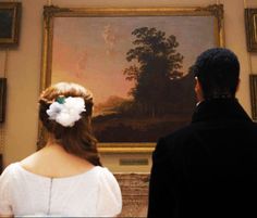 a man and woman standing in front of a painting with flowers in their hair looking at each other